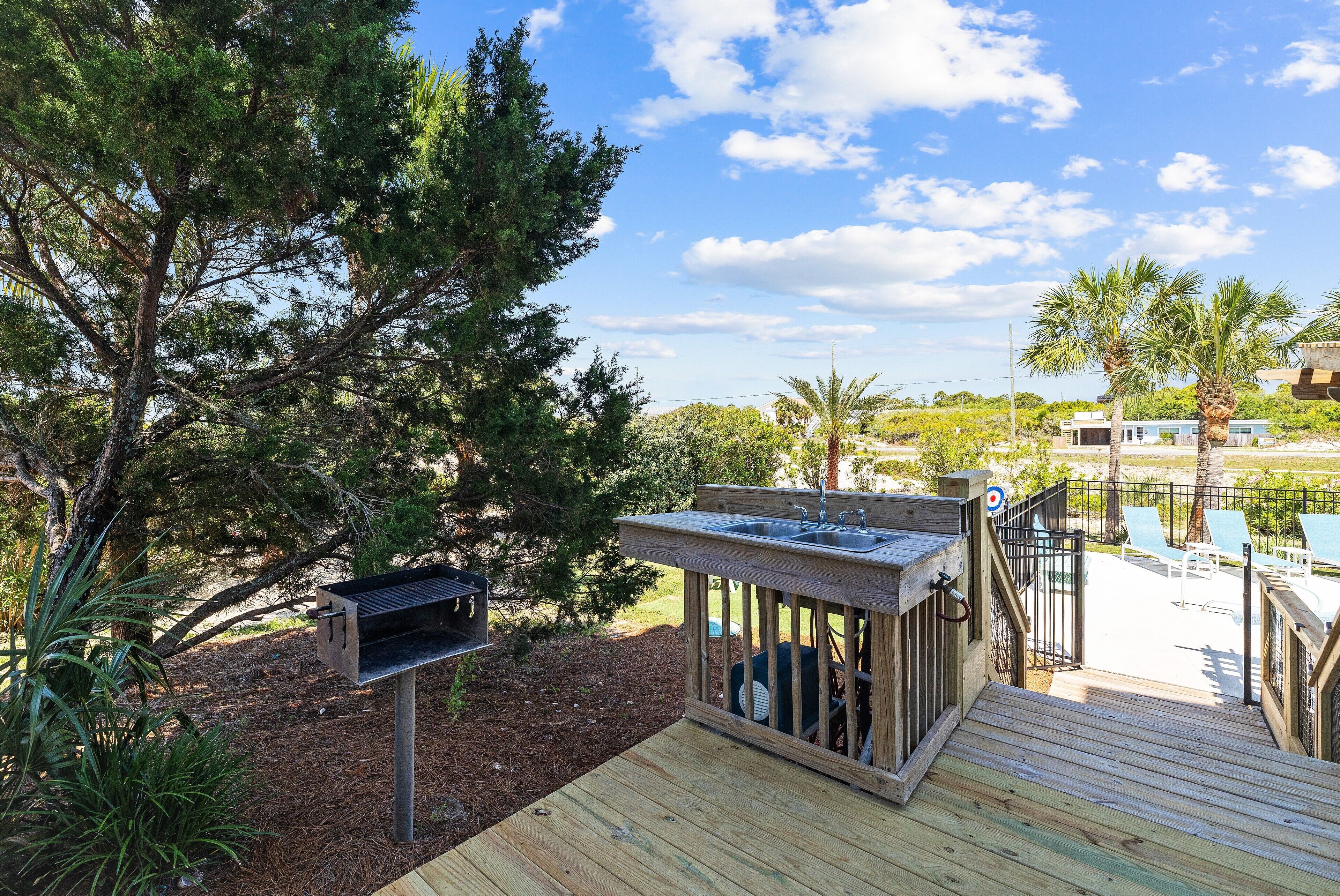 Una terraza de madera con una parrilla y un lavadero, rodeada de árboles y una zona de piscina.