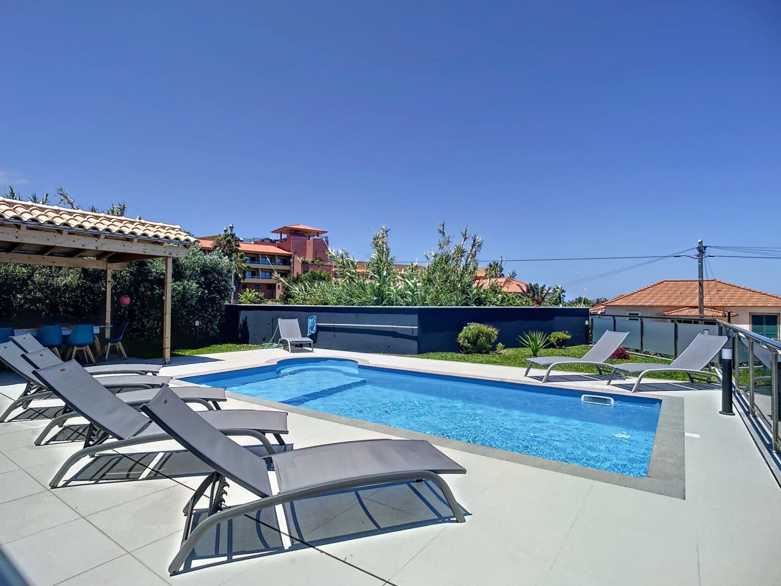 A swimming pool with lounge chairs, a covered seating area, and a view of buildings in the background.