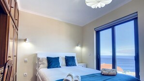 Ein Schlafzimmer mit einem großen Bett, zwei Nachttischen, einem Kleiderschrank und einem großen Fenster mit Meerblick.