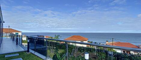 A modern balcony with glass railings overlooking a coastal view.