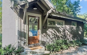 A small, single-story building with a wooden door and windows, a number '142' on the door, and a small porch area.