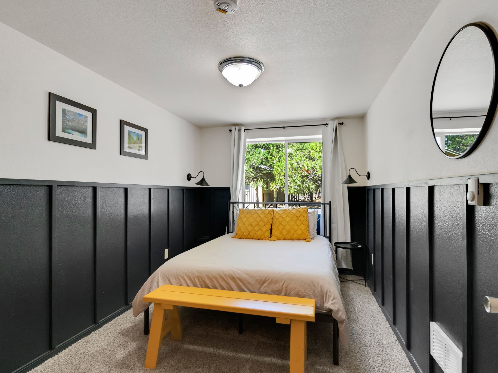 A bedroom with a bed, a bench, a window with a view of trees, and a ceiling light.