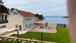 A stone building with a red roof, a patio with a wooden pergola, and a view of a lake. - Villa Diocletian***** Solta, Premium traditional stone house next to the sea (Rogac)