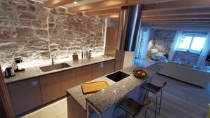 A modern kitchen with a stone wall, stainless steel appliances, and a bar area with stools. - Villa Diocletian***** Solta, Premium traditional stone house next to the sea (Rogac)