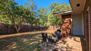 Patio trasero con zona de estar, una parrilla y una valla de madera.