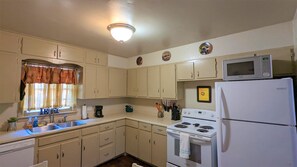 Una cocina pequeña con armarios blancos, estufa, microondas y refrigerador.