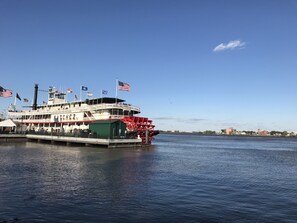 Un grand bateau fluvial à plusieurs ponts, arborant des drapeaux américains, est amarré à un quai, avec une vue sur la ville en arrière-plan.