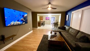 Una sala de estar con un televisor de pantalla plana, un sofá de cuero, una mesa de centro de madera y un ventilador de techo.