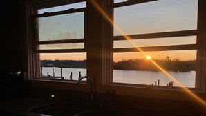 Una cocina con un lavamanos y vista a un atardecer sobre el agua.