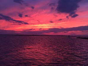 Un coucher de soleil sur une étendue d'eau calme, avec une côte lointaine à l'horizon.