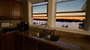 Una cocina con un lavamanos doble, armarios de madera y vistas a un lago al atardecer.