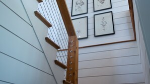 Een trap met houten leuningen en een dakraam, die leidt naar een kamer met witte wanden en ingelijste botanische prints.
