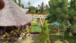 A thatched-roof structure with outdoor seating, a pool, and lush greenery. - MODERN SOUTH HOTEL (Diani Beach)
