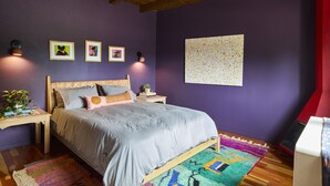 A bedroom with a wooden bed, purple walls, and a ceiling fan. There are framed pictures on the wall and a colorful rug on the floor. - Luxurious 1bd Charmer  `Poni Suite` @ La Dea (Santa Fe)