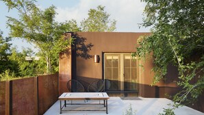 A modern outdoor patio with a table and chairs, a glass door, and a brown wall. - Bright, Playful 2bd `Atami Suite` @ La Dea (Santa Fe)