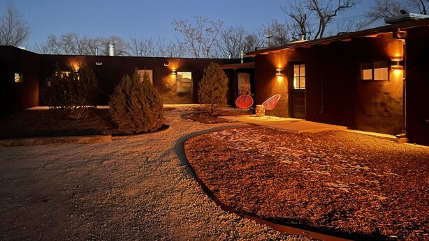 A building with a gravel driveway, a pathway, and a small garden area with a tree and two red chairs. - Bright, Playful 2bd `Atami Suite` @ La Dea (Santa Fe)