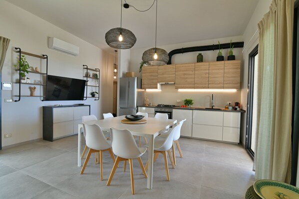 Una cocina moderna con armarios blancos, una mesa de comedor con sillas e iluminación colgante.