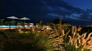 Une vue nocturne d’un complexe hôtelier avec des espaces de détente en plein air, une piscine et une vue sur les gratte-ciel de la ville.