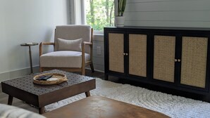 A living room with a beige armchair, a wooden coffee table, a white shag rug, and a black cabinet with woven doors. - Romantic Retreat | Dual-Head Shower for Two (Sautee)