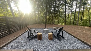 An outdoor seating area with two Adirondack chairs, a fire pit, and a wooden table. - Romantic Retreat | Dual-Head Shower for Two (Sautee)