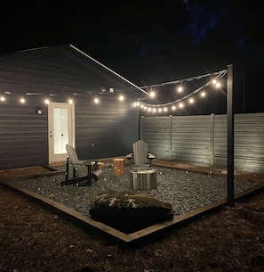 Ein Garten mit einer Holzterrasse, einer Feuerstelle, Lichterketten und einem Stuhl.