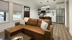 A modern living room with a brown sectional sofa, a coffee table, and a view of the kitchen in the background. - Romantic Retreat | Dual-Head Shower for Two (Sautee)