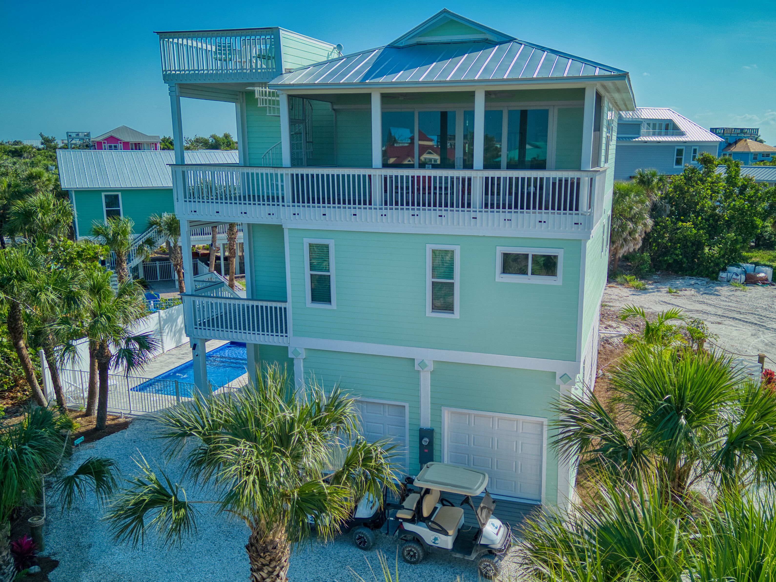 A multi-story house with a pool, a golf cart, and palm trees.