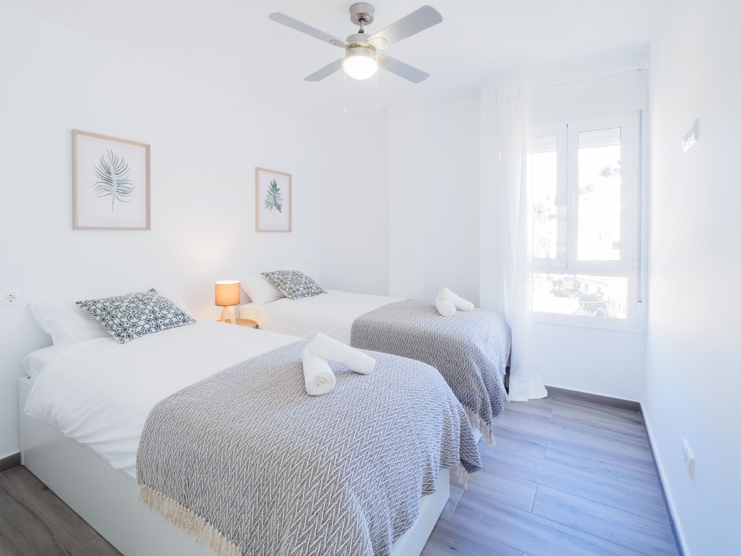 A bedroom with two beds, a ceiling fan, and framed leaf artwork on the wall.
