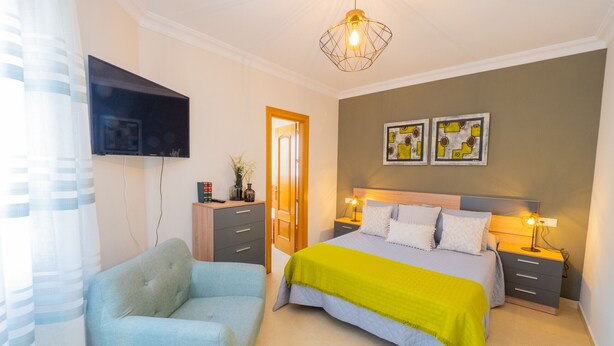 A bedroom with a bed, bedside tables, a TV mounted on the wall, and a door leading to another room.