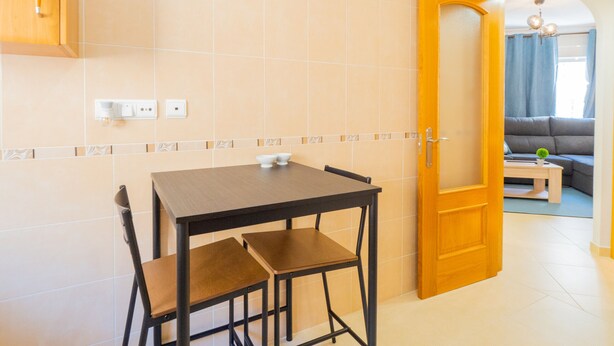 A compact kitchen with a dining table and chairs, a wooden door leading to a living area with a sofa and a small table. - Cubo's Liberty Apartment / free wifi / urban / family / teleworking (Alhaurín el Grande)