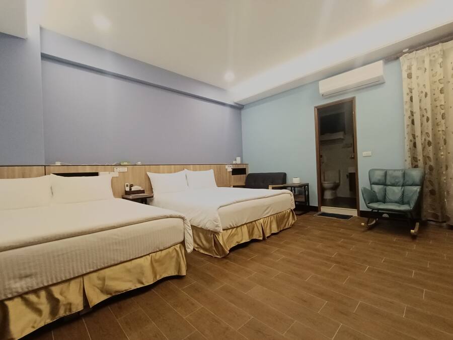 Habitación de hotel con dos camas, un escritorio, una silla, un equipo de aire acondicionado y una puerta que da a un baño.