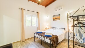 A bedroom with a bed, a window with curtains, a wall-mounted air conditioner, a hanging light fixture, and a painting of a sunset over water. - Cubo's Casa Rural Marifran / Private pool / Air conditioning (Alhaurín el Grande)