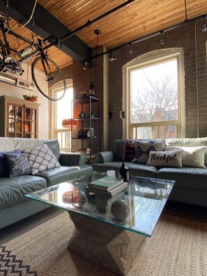 A modern living room with a glass coffee table, leather sofas, and a large window providing natural light. - 1+1 heritage loft in trendy dt Toronto (Toronto)