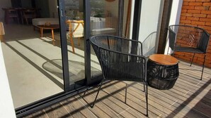 Un patio moderno al aire libre con terraza de madera, sillas de metal negro y una pequeña mesa redonda.