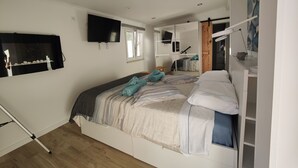 A bedroom with a bed, a TV mounted on the wall, a window, and a mirror.