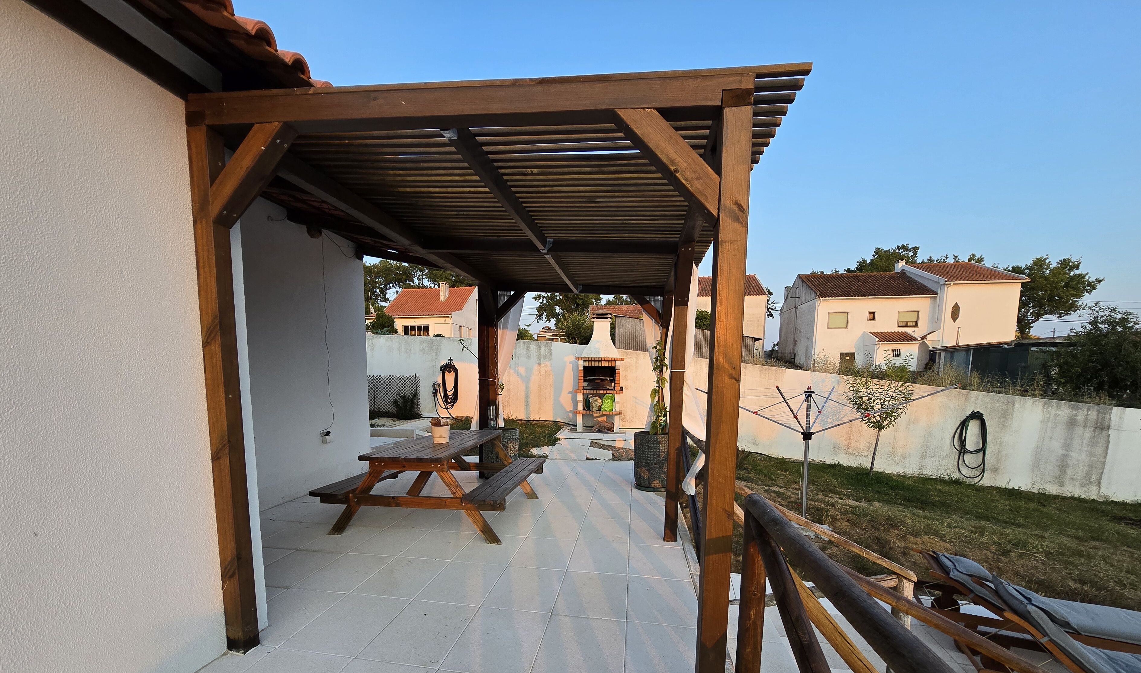 A covered patio with a wooden pergola, a picnic table, and a barbecue grill.