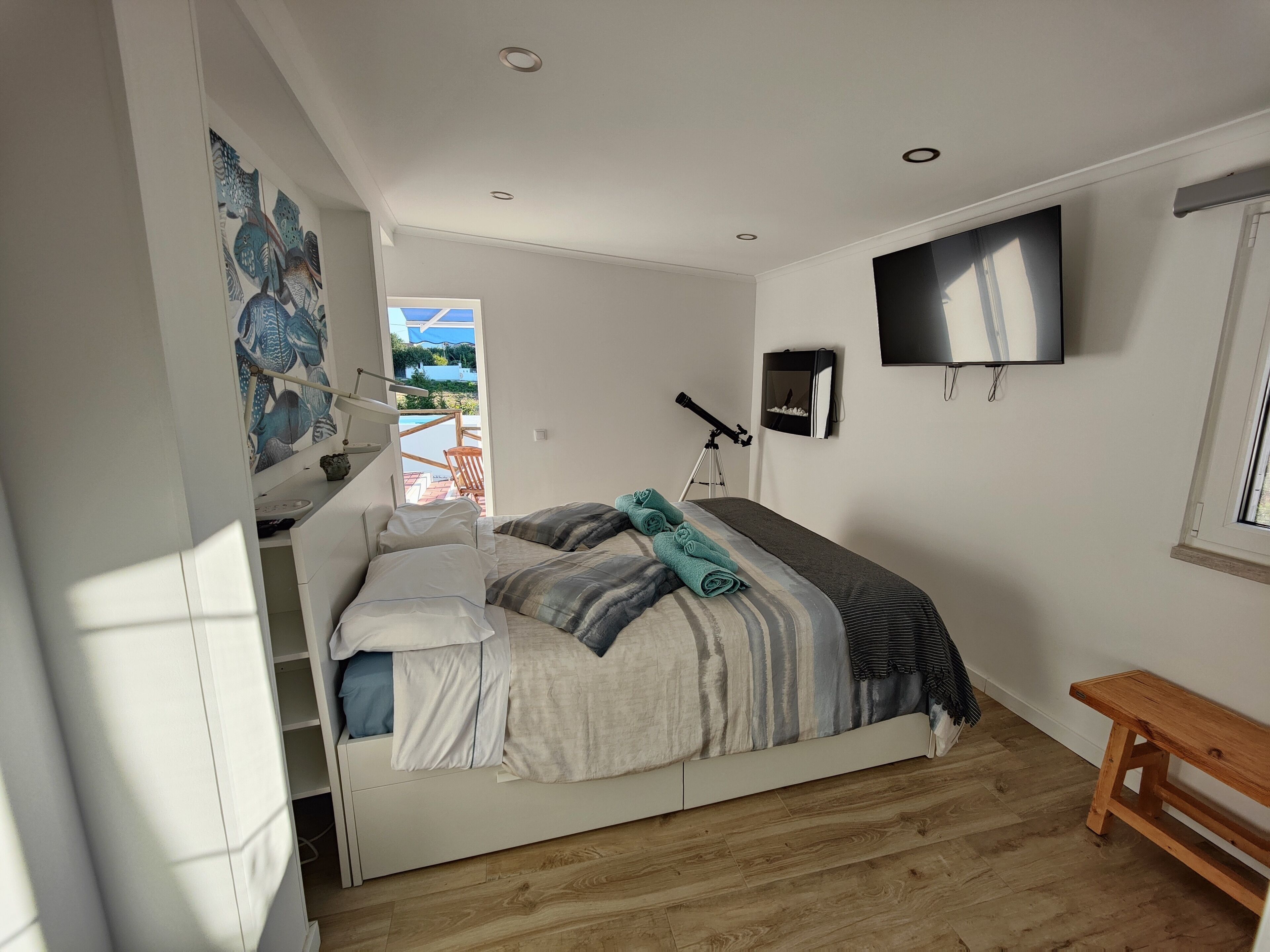 A bedroom with a bed, a telescope, a TV, and a window.