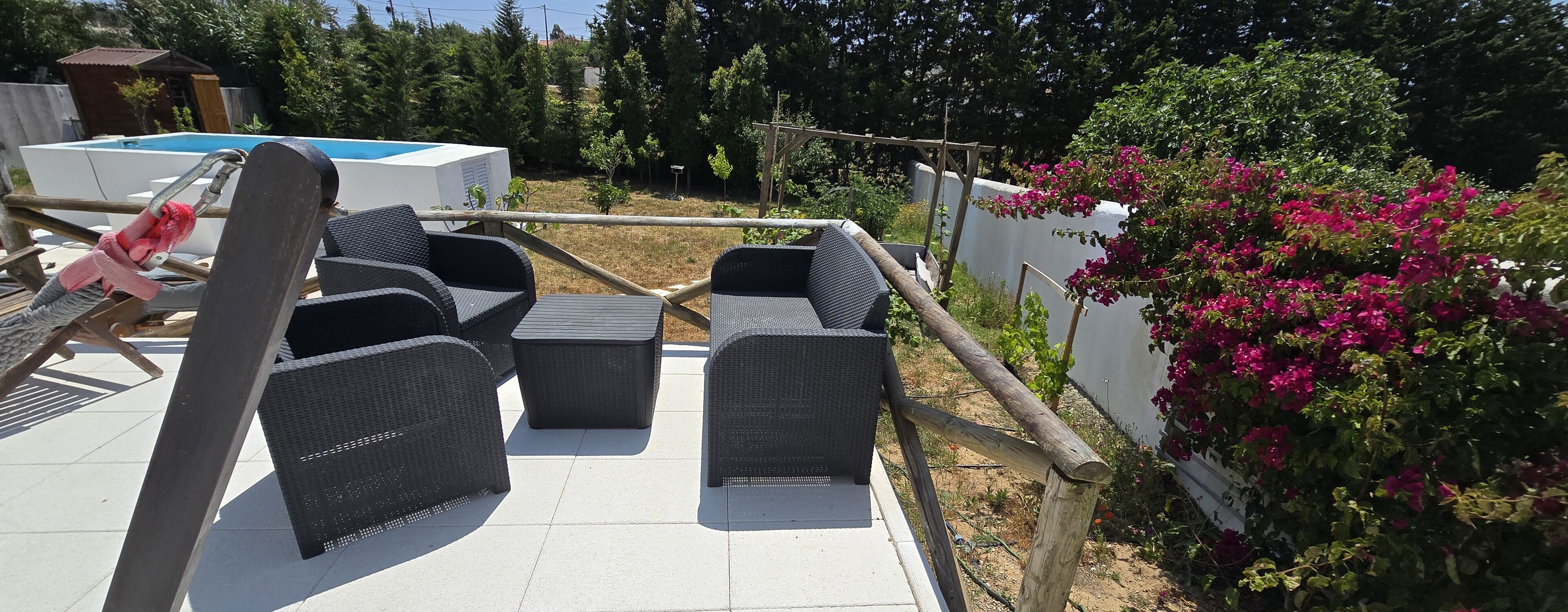 An outdoor seating area with wicker furniture, a pool, and a garden with bougainvillea.