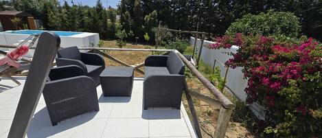 An outdoor seating area with wicker furniture, a pool, and a garden with bougainvillea.
