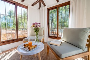 Une pièce avec un canapé, une table avec des croissants et du jus, et un vase rempli de fleurs.