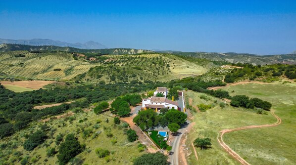 Un vaste domaine dont le bâtiment principal est entouré d’une végétation luxuriante et de collines ondoyantes.