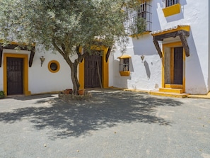 A courtyard with a tree, a building with yellow and white walls, and a wooden door. - Cubo's Cortijo El Perezon / rural / private pool / air conditioning (Archidona)