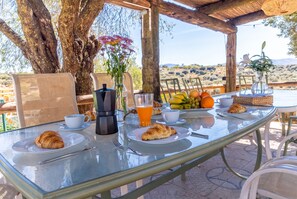 Un coin petit-déjeuner aménagé à l’extérieur, avec une table, des chaises et une vue sur le paysage.