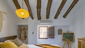 Een slaapkamer met een bed, een hanglamp, een schilderij aan de muur en een raam.