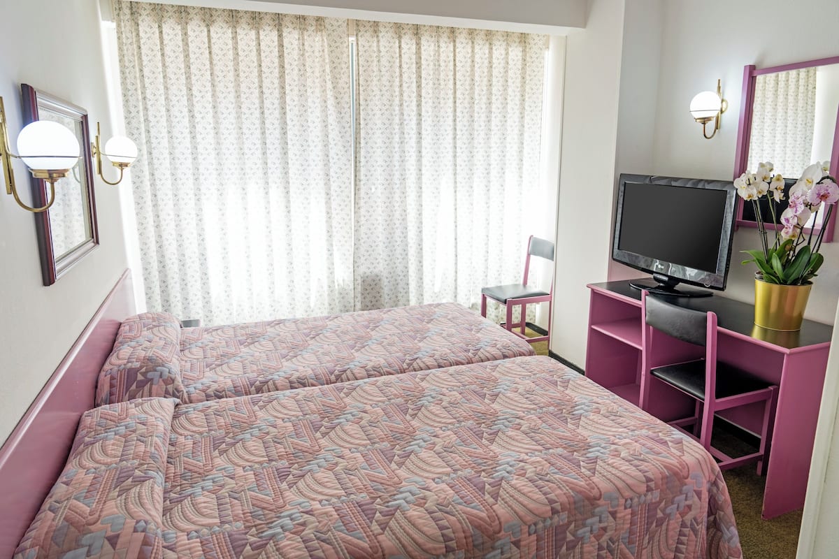 Habitación de hotel con dos camas, televisión, escritorio, silla y ventana con cortinas.