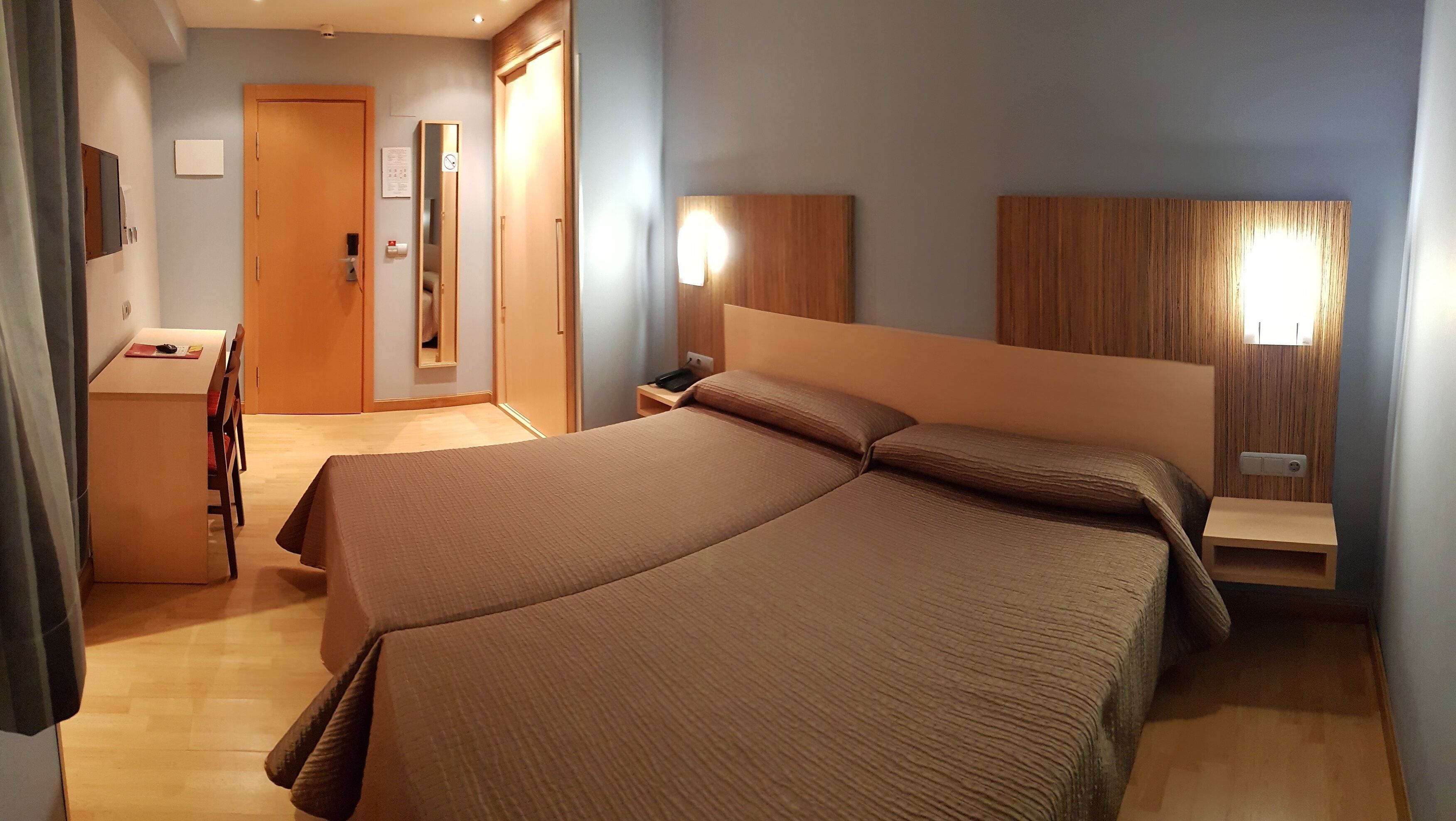 A hotel room with a bed, bedside tables, a desk, and a mirror.