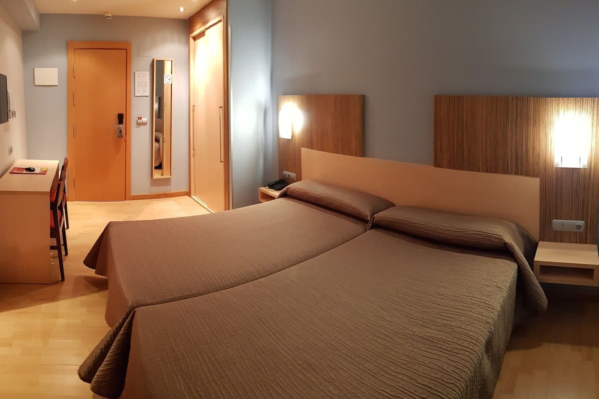 Una habitación de hotel con una cama, mesitas de noche, un escritorio y un espejo.