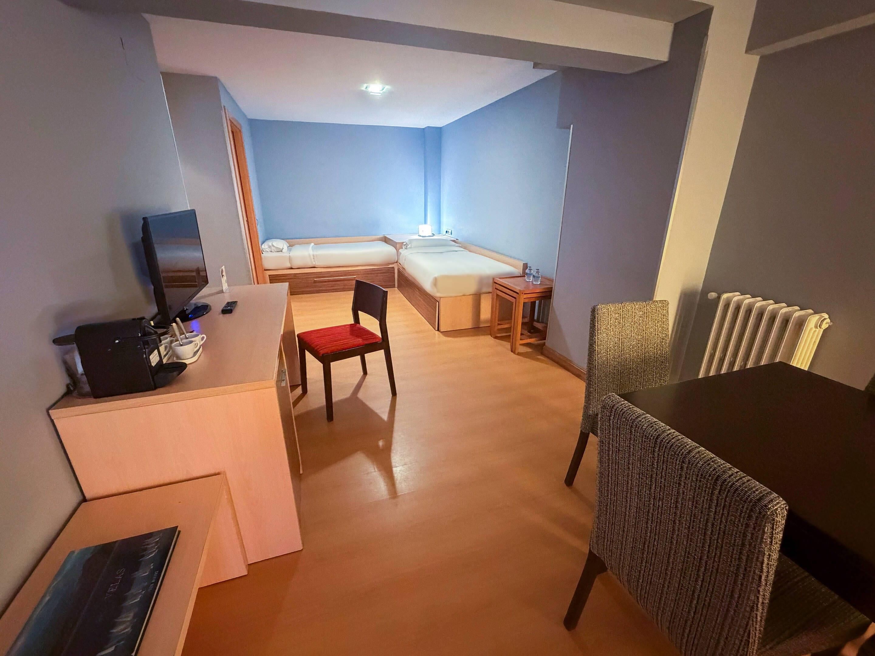 Una habitación de hotel con cama, escritorio, silla, mesa y radiador.