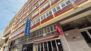 Et hotel med flere etager, et tydeligt skilt med 'FALISAS HOTEL', store vinduer og en facade i rødt og gult.