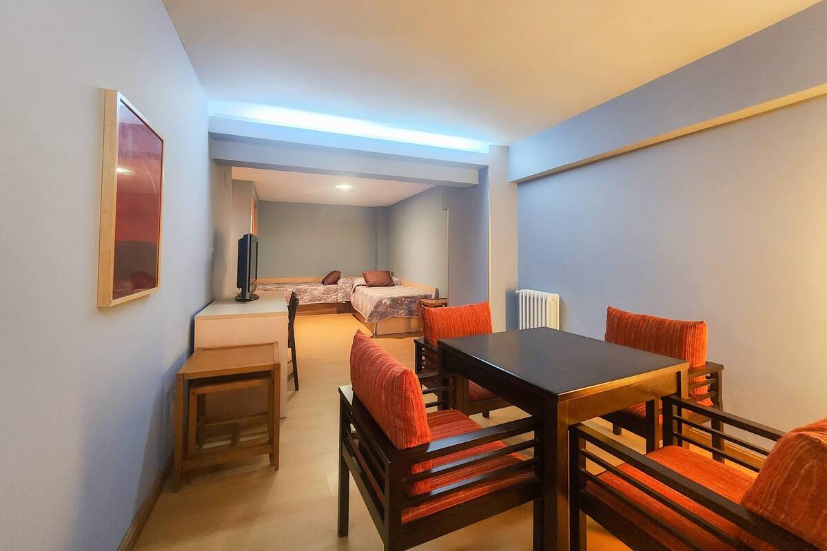 A hotel room with a bed, a desk, a chair, a table, and a radiator.